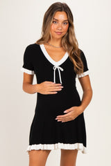woman wearing a black ribbed maternity dress with white trim and a tie detail, cradling her baby bump
