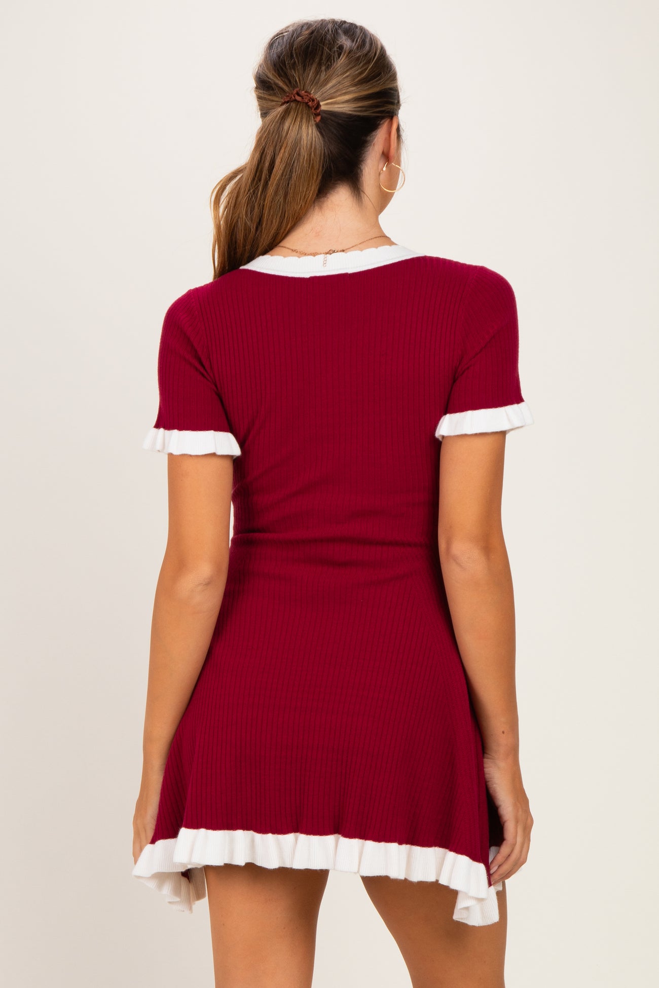 woman wearing a burgundy maternity dress with white ruffle trim on sleeves and hem, shown from the back