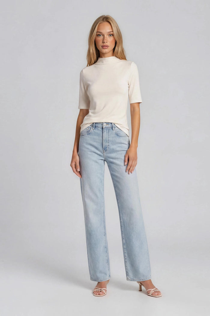 woman wearing a cream short sleeve mock neck top and light blue wide leg jeans with heeled sandals.