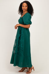 woman wearing a green maxi dress with puff sleeves and lace detailing, standing sideways on a light background