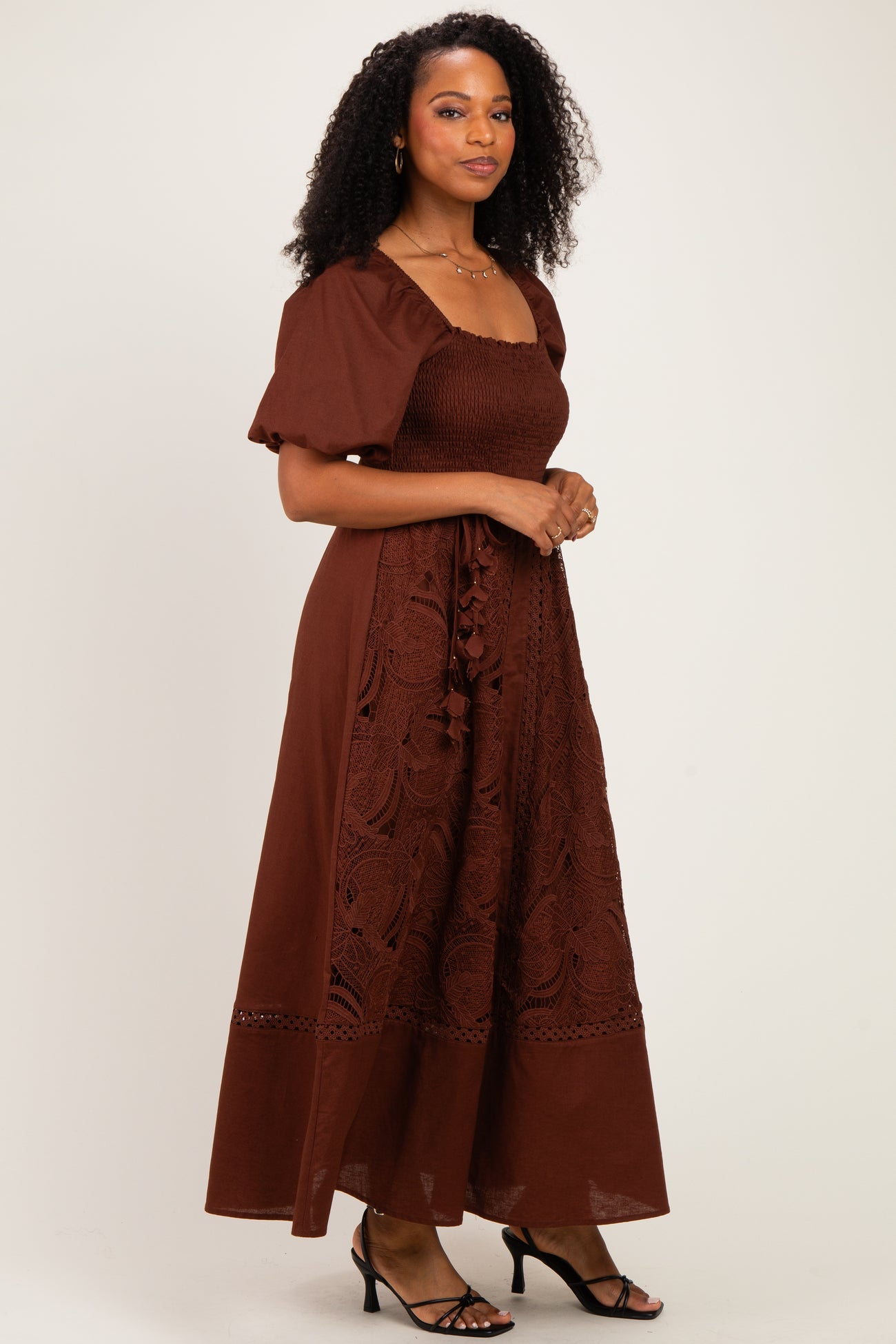 woman wearing a brown maxi dress with puff sleeves and embroidered details, standing against a neutral background