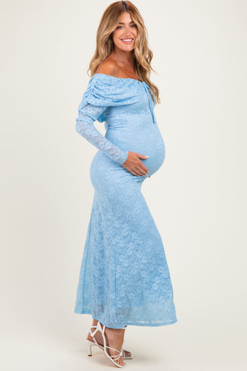 woman wearing a light blue off-the-shoulder lace maternity dress and gently holding her baby bump