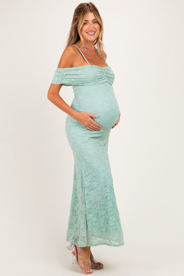 woman wearing a light teal off-the-shoulder lace maternity dress and holding her baby bump