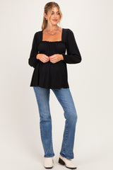 woman wearing a black maternity top with long sleeves and a flared hem, showcasing her baby bump, paired with blue jeans