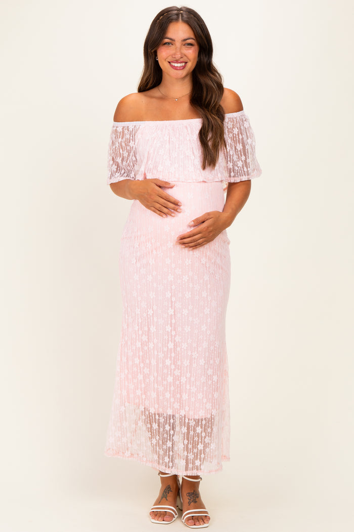 woman wearing a light pink off-the-shoulder lace maternity dress and holding her baby bump