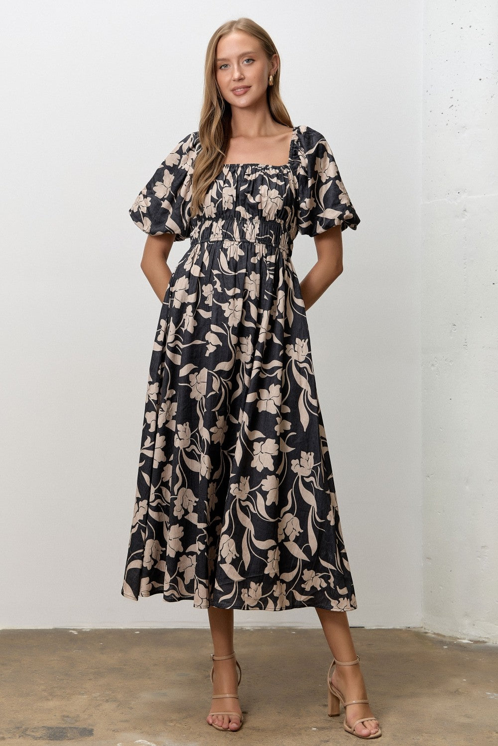 woman wearing a black floral midi dress with puff sleeves and a smocked bodice, standing with hands in pockets