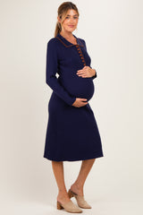woman wearing a navy blue ribbed maternity dress with a buttoned collar and holding her baby bump