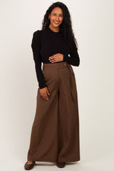woman wearing a black long sleeve top and brown wide leg maternity pants, holding her baby bump