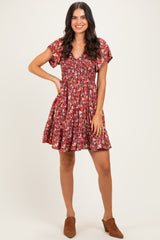 woman wearing a red floral short sleeve dress with a smocked bodice and a flared skirt, standing with one hand on her hip