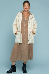woman wearing a cream oversized jacket over a brown checkered maternity dress, with black ankle boots