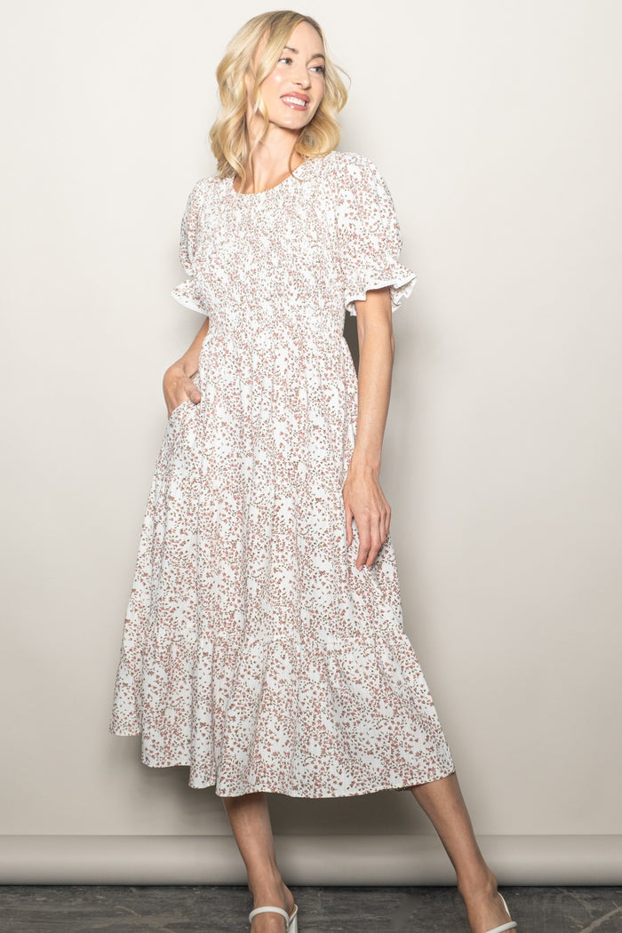 woman wearing a white floral midi dress with puff sleeves and gathered detailing, standing with a smile