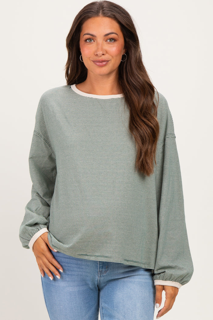 woman wearing a green striped maternity top with long sleeves and a relaxed fit, styled with light blue jeans