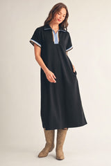 woman wearing a black polo-style dress with a blue and white collar, standing in brown cowboy boots