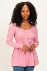 woman wearing a pink ribbed long sleeve top with a scoop neckline and button details, styled with a flared hem