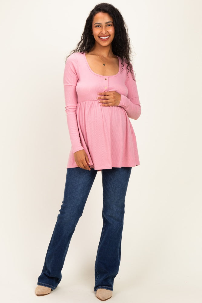 woman wearing a pink long sleeve maternity top with buttons and a baby bump, paired with blue flared jeans