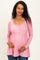 woman wearing a light pink maternity top with buttons, gently hugging her baby bump and smiling