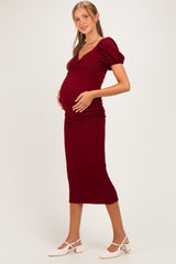 woman wearing a burgundy fitted maternity dress with puff sleeves and side ruching, showcasing her baby bump