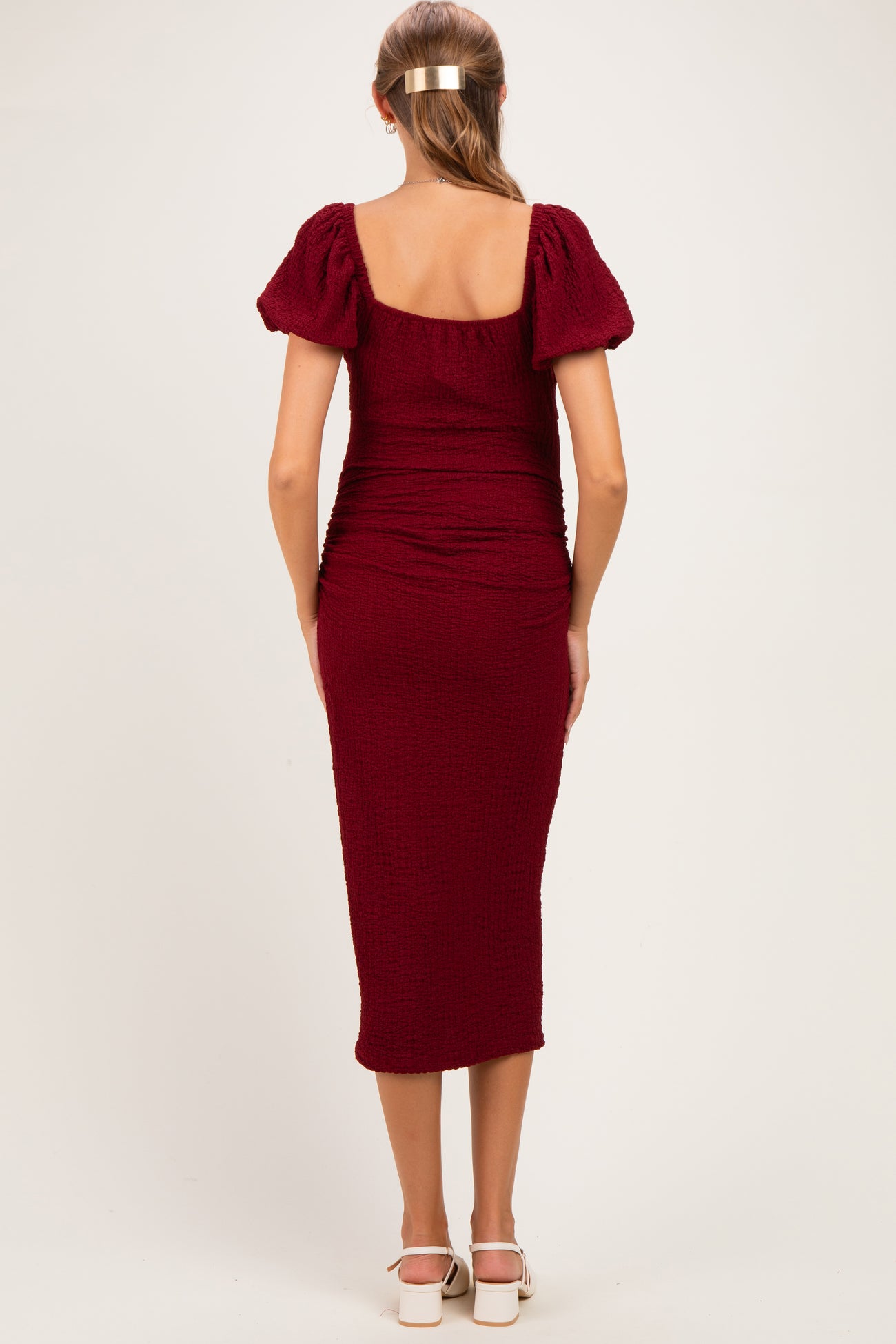 woman wearing a burgundy maternity dress with puff sleeves and a midi length, showing a fitted silhouette from the back