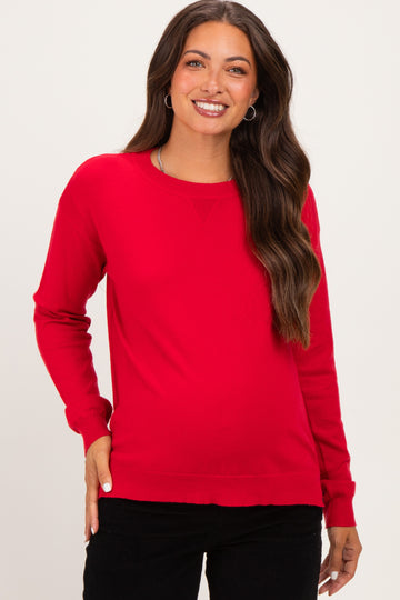 woman wearing a bright red long sleeve maternity sweater with a relaxed fit and smiling at the camera
