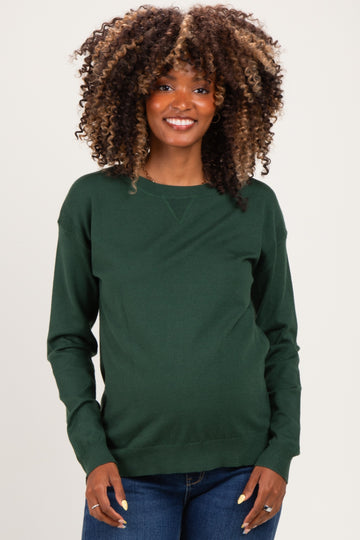 woman wearing a dark green long sleeve maternity sweater and smiling while showing her baby bump