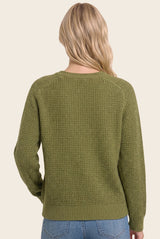 woman wearing a green textured knit sweater, shown from the back, styled with light blue jeans