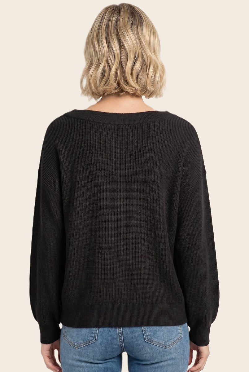 woman wearing a black oversized sweater with a textured knit and long sleeves, viewed from the back