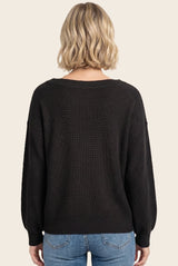 woman wearing a black oversized sweater with a textured knit and long sleeves, viewed from the back
