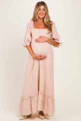 woman wearing a blush floral maternity maxi dress with puff sleeves and ruffled hem, holding her baby bump