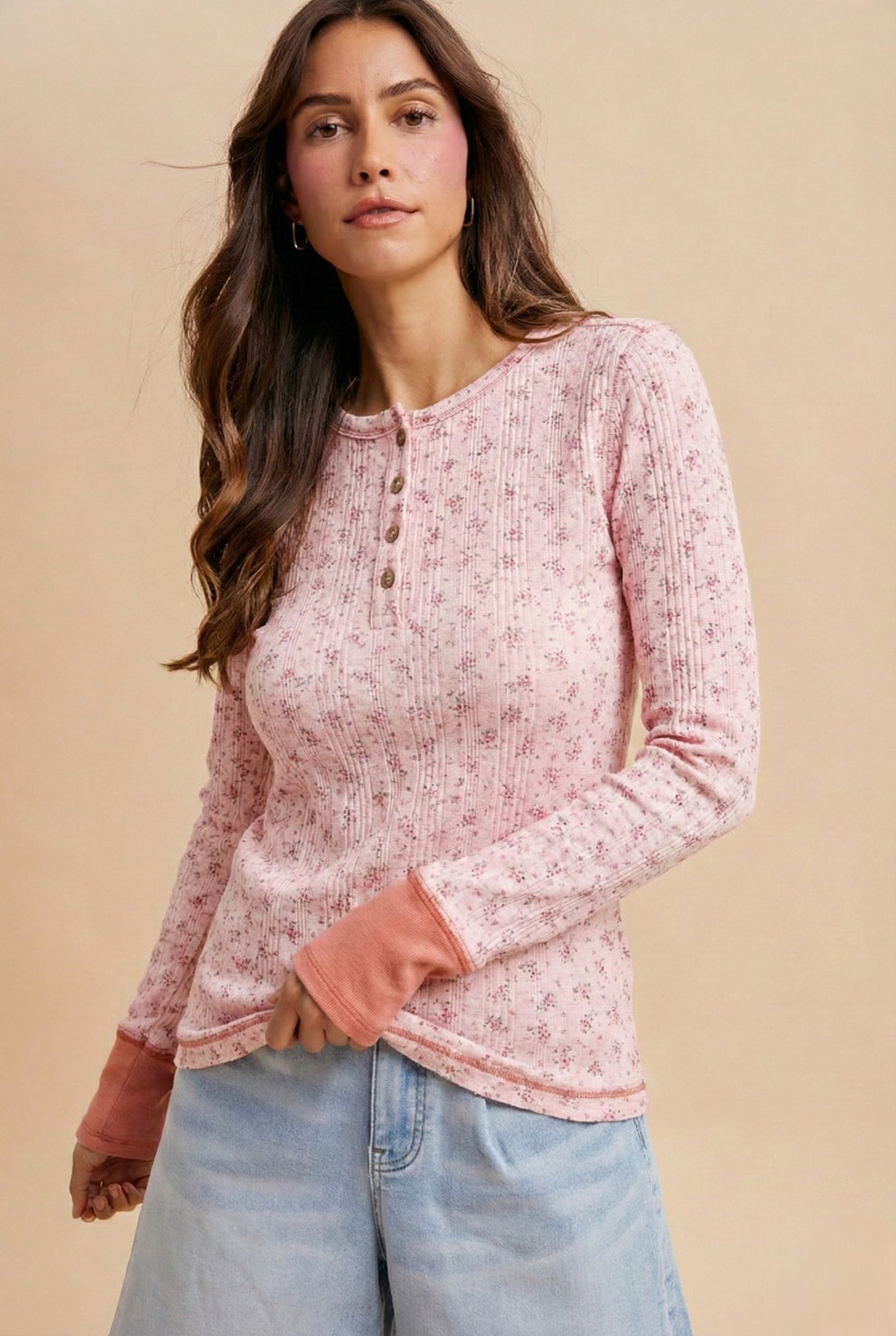 woman wearing a pink floral long sleeve henley top with button details and contrast cuffs, paired with light blue jeans