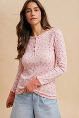 woman wearing a pink floral long sleeve henley top with button details and contrast cuffs, paired with light blue jeans