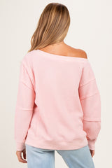 woman wearing a pink off-the-shoulder maternity sweater with a relaxed fit and long sleeves
