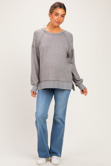 woman wearing a gray ribbed maternity sweatshirt with side slits, paired with light blue flared jeans and white sneakers