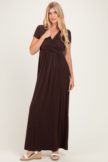 woman wearing a chocolate brown short sleeve maxi dress with a twisted bodice and posing with one hand on her hip