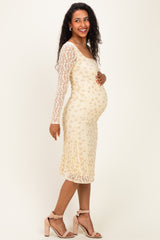 woman wearing a cream lace long sleeve maternity dress and holding her baby bump