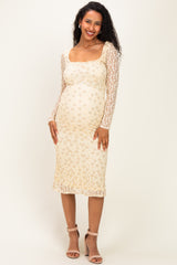 woman wearing a beige floral lace maternity dress with long sleeves and a visible baby bump