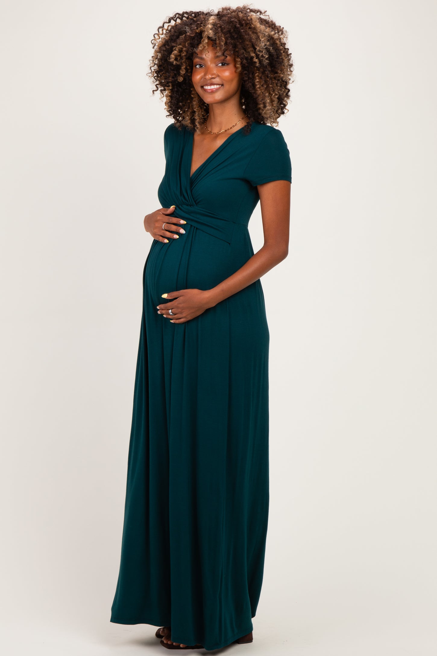 woman wearing a dark green short sleeve maternity maxi dress and gently holding her baby bump