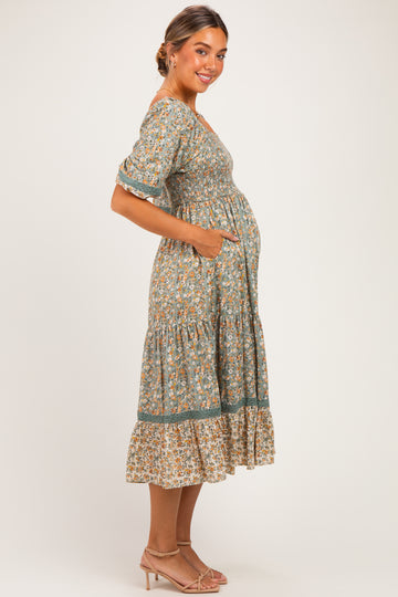 woman wearing a green floral maternity dress with pockets and tiered hem, highlighting her baby bump