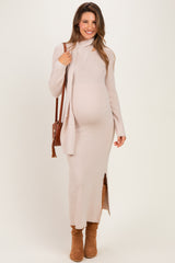 woman wearing a light beige ribbed maternity maxi dress with a side slit and a matching long cardigan, holding a brown purse and showing her baby bump