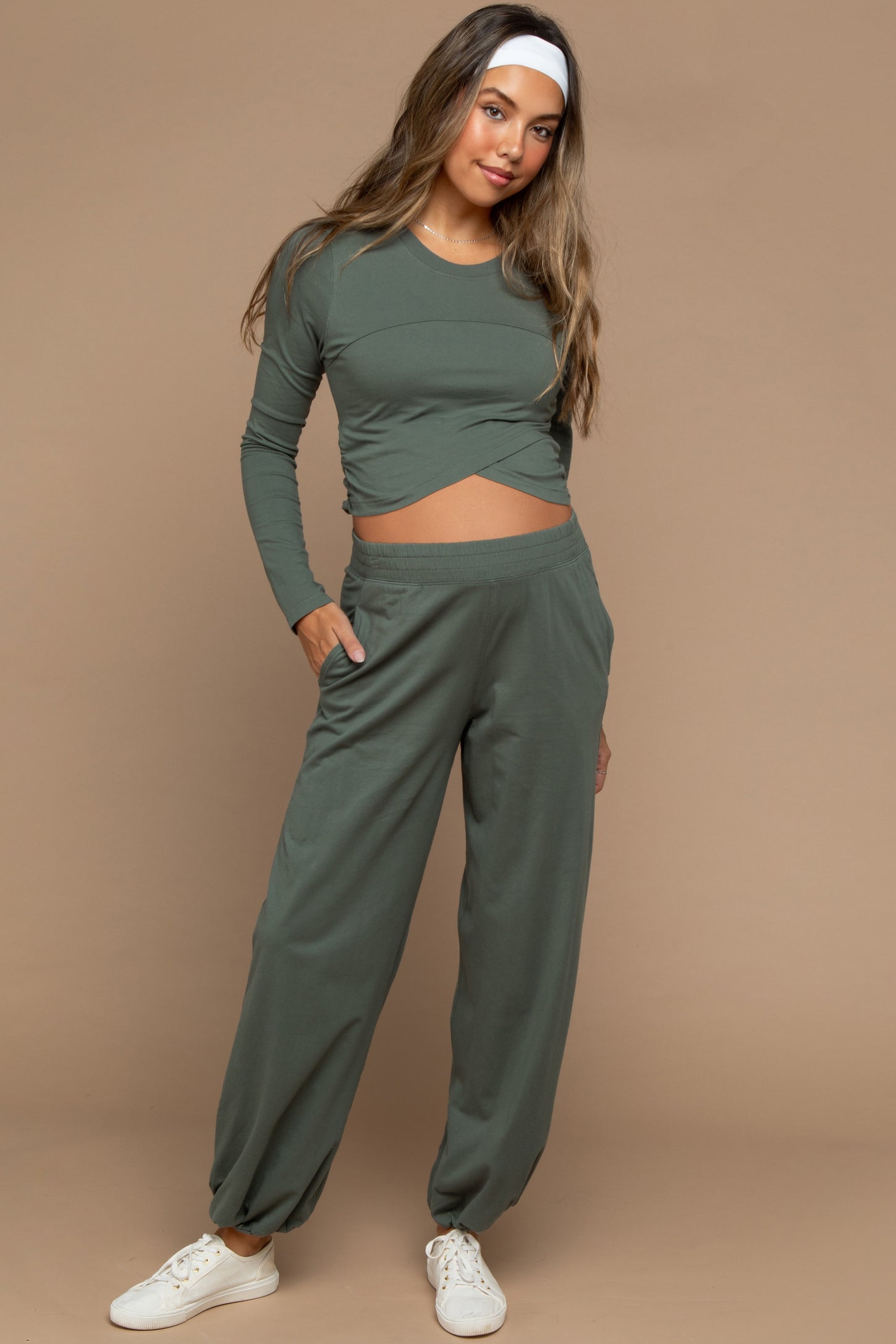 woman wearing a green maternity long sleeve top with a twist front and matching jogger pants, showing her baby bump