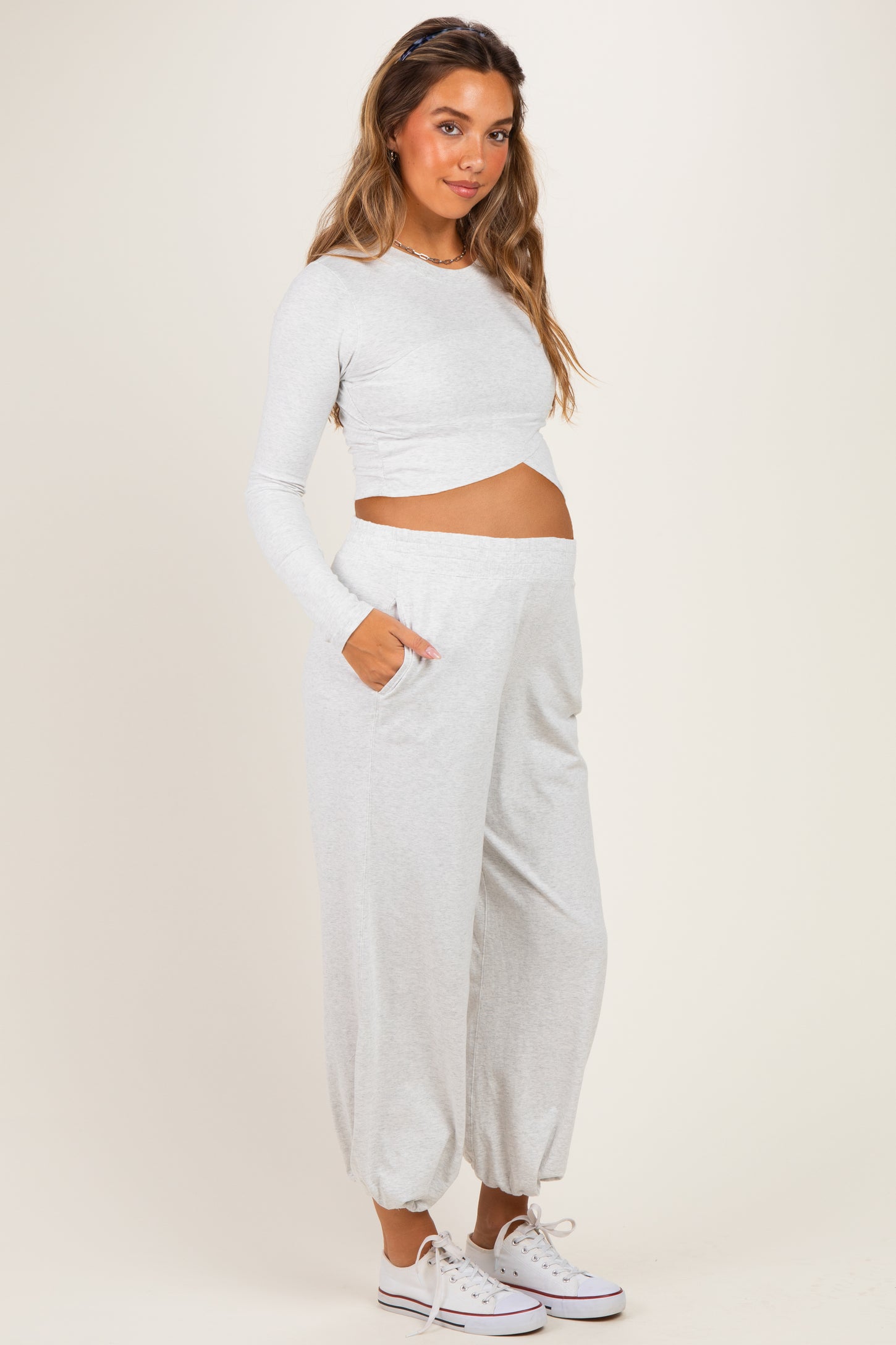 woman wearing a light gray long sleeve maternity top and matching pants, highlighting her baby bump