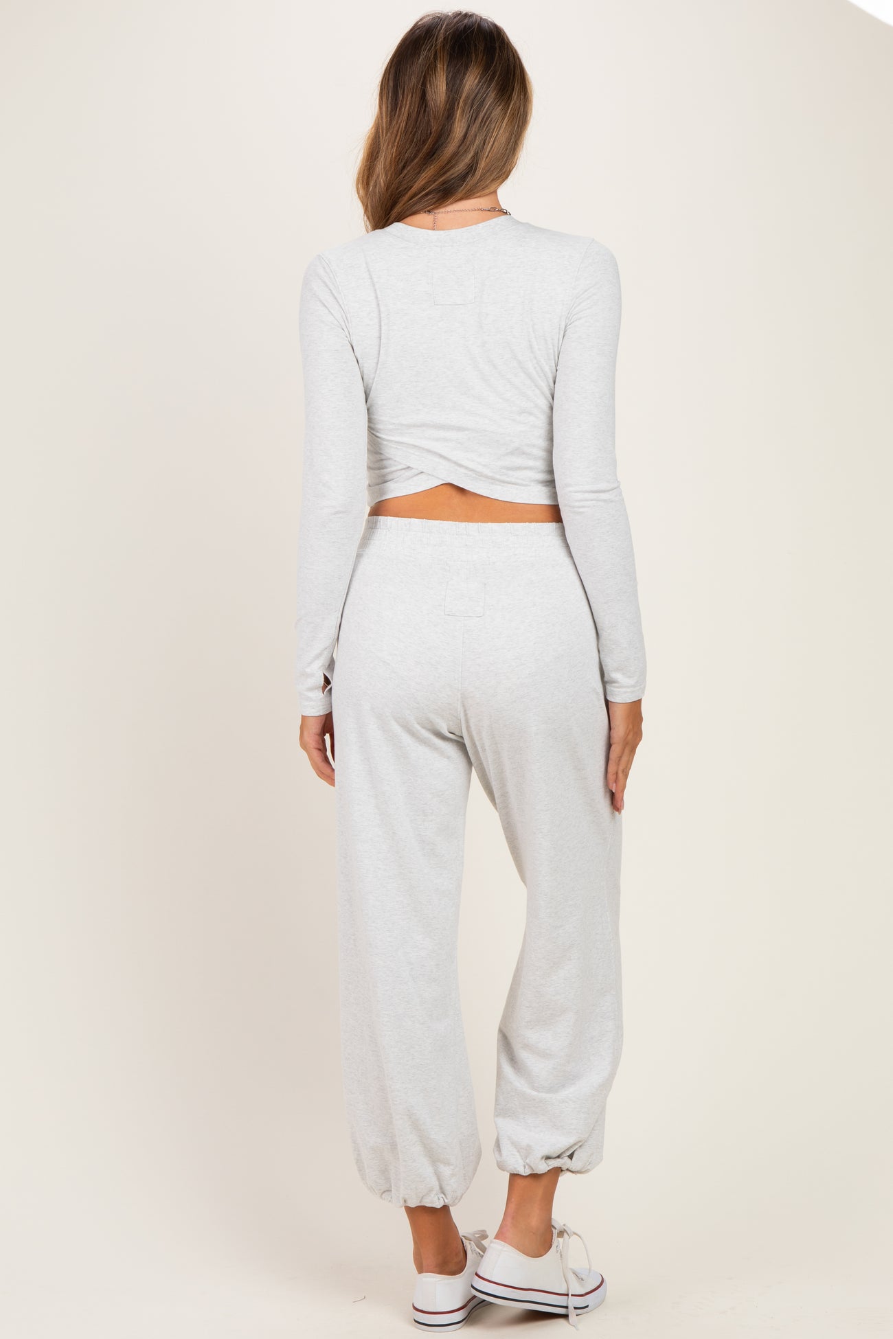 woman wearing a light gray maternity long sleeve crop top and matching jogger pants, showing a baby bump
