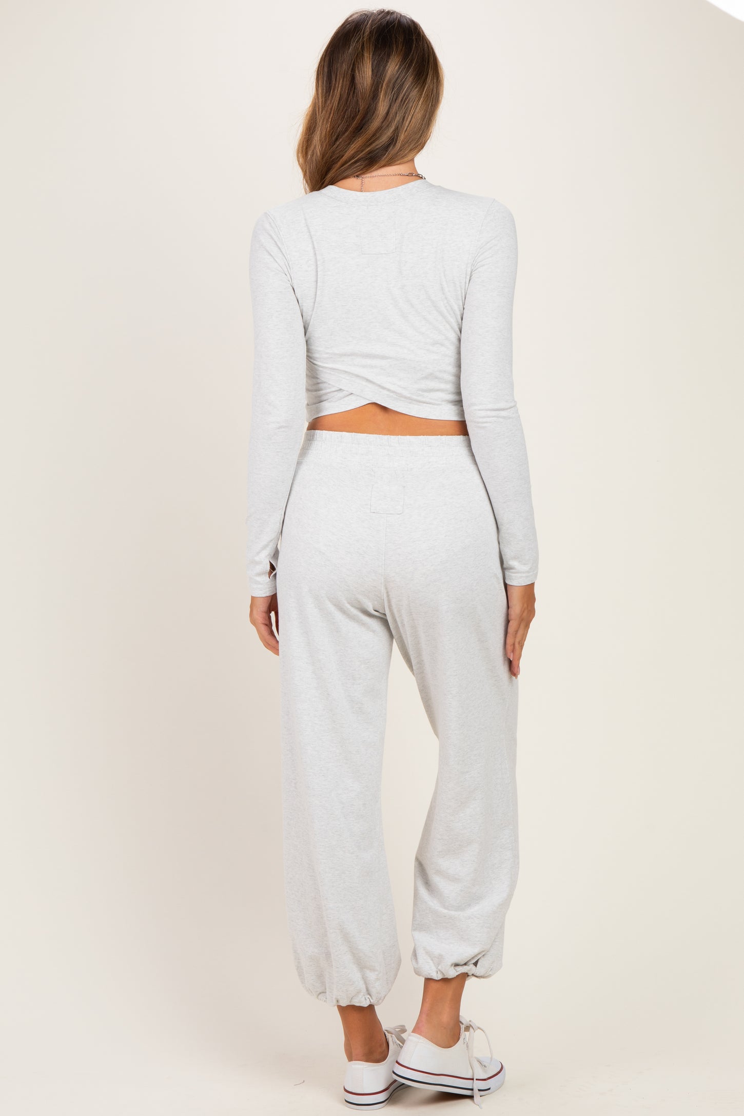 woman wearing a light gray maternity long sleeve crop top and matching jogger pants, showing a baby bump