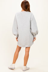 woman wearing a light grey oversized sweatshirt dress with balloon sleeves and white sneakers, viewed from the back