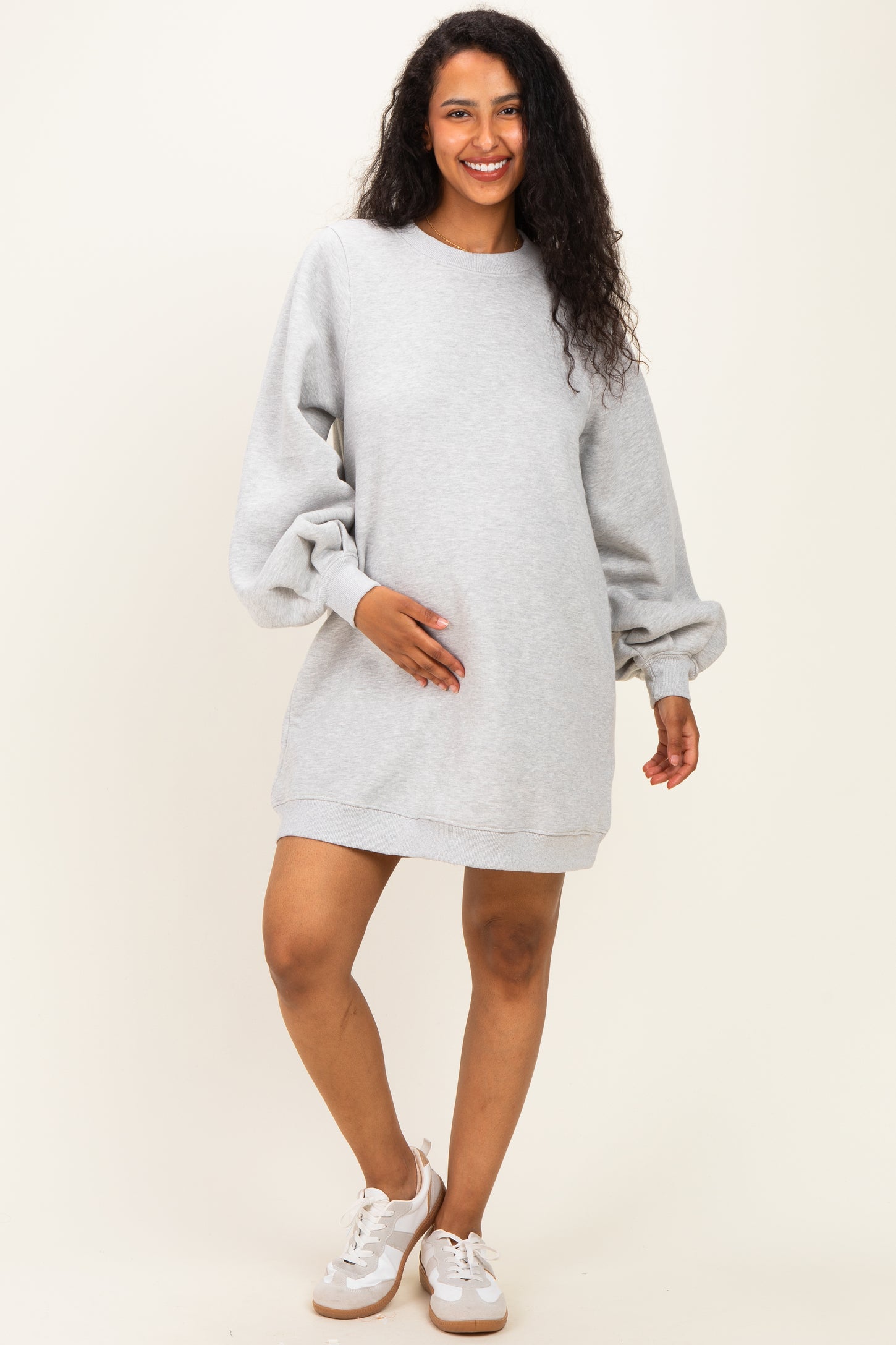 woman wearing a light gray oversized maternity sweatshirt dress and gently holding her baby bump