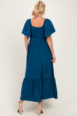 woman wearing a teal off-the-shoulder maxi dress with flutter sleeves and a tiered skirt, seen from the back