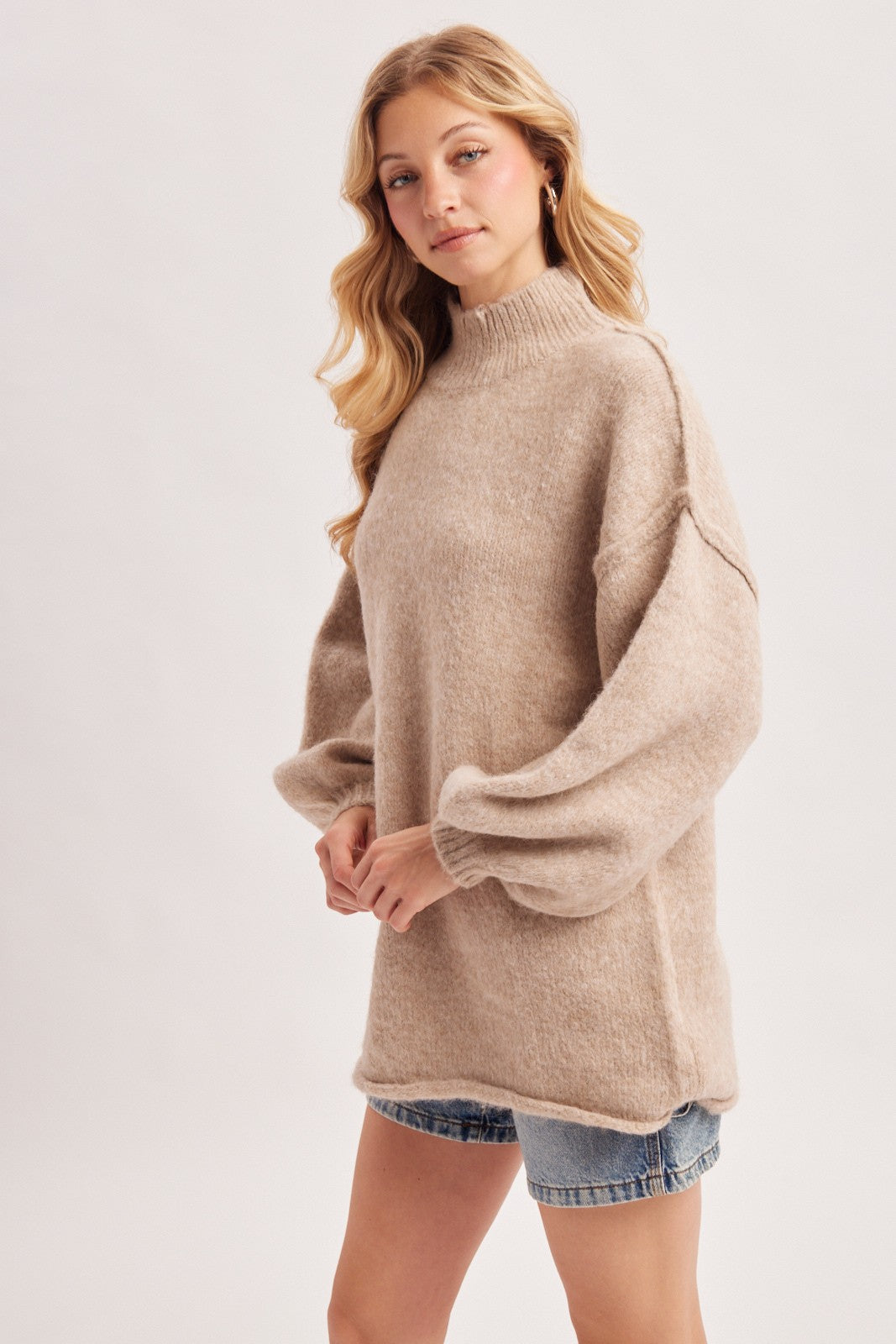 woman wearing a beige oversized sweater with balloon sleeves and a mock neck, paired with denim shorts