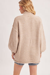 woman wearing a beige oversized sweater with a high collar and balloon sleeves, styled with denim shorts.
