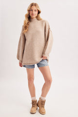 woman wearing a cozy beige oversized sweater with a high neck, paired with denim shorts and tan ankle boots