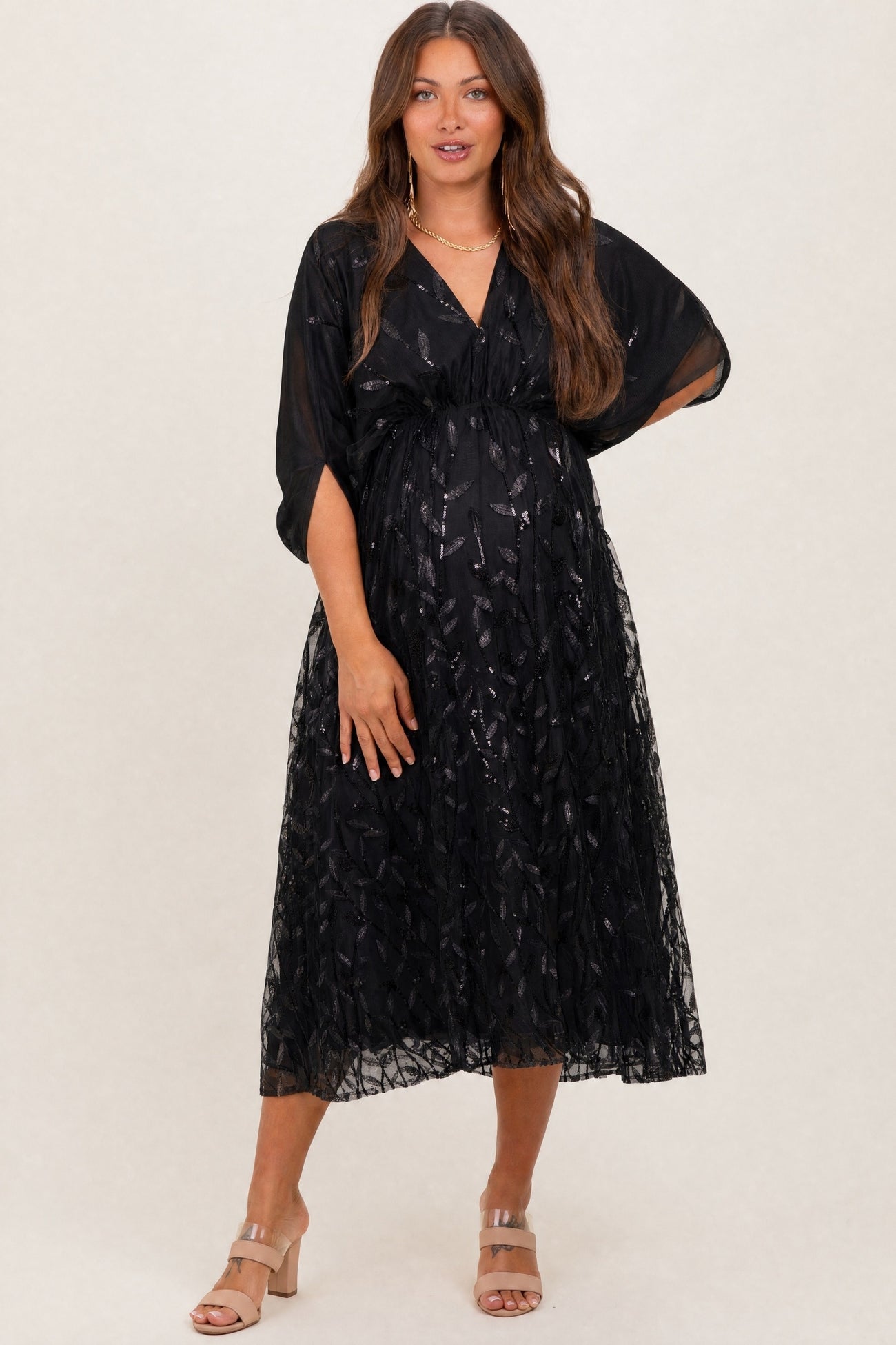 woman wearing a black maternity dress with sheer overlay and short sleeves, displaying her baby bump