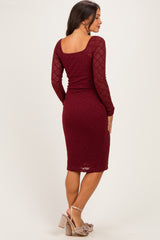 woman wearing a burgundy lace maternity dress with long sleeves and a square neckline, showing a fitted silhouette